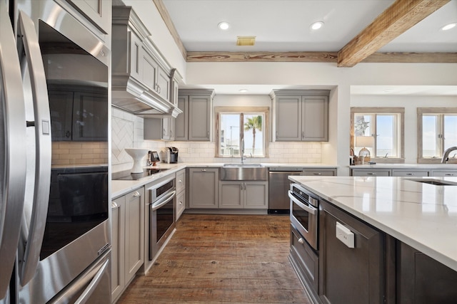 kitchen with sink, backsplash, stainless steel appliances, beamed ceiling, and dark wood-type flooring