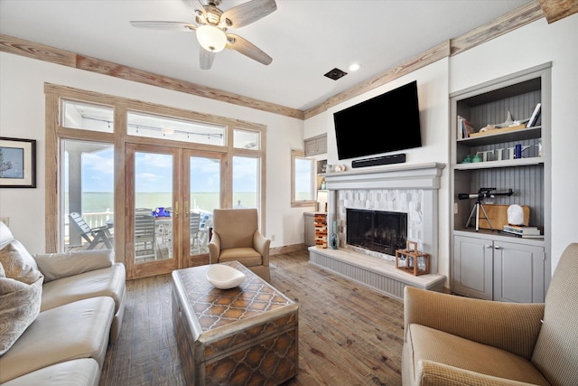 living room with ceiling fan, dark hardwood / wood-style flooring, a brick fireplace, built in features, and french doors