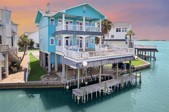 rear view of house with boat lift, a patio, a water view, and a balcony