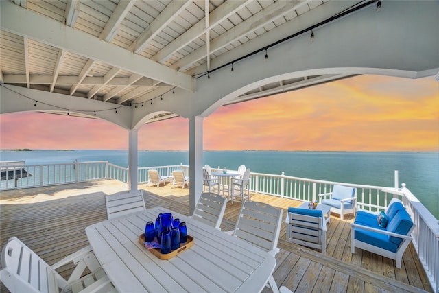 deck at dusk with outdoor lounge area and a water view