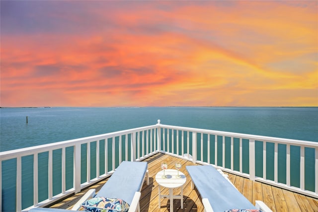 balcony at dusk featuring a water view