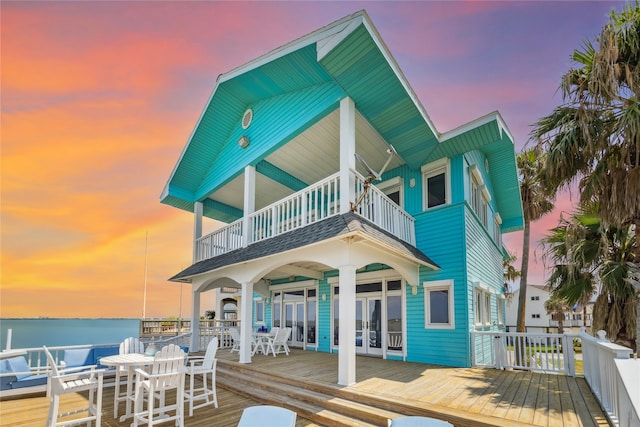 back house at dusk featuring a balcony and a deck with water view