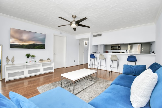 living room featuring ceiling fan, wood-type flooring, ornamental molding, and a textured ceiling