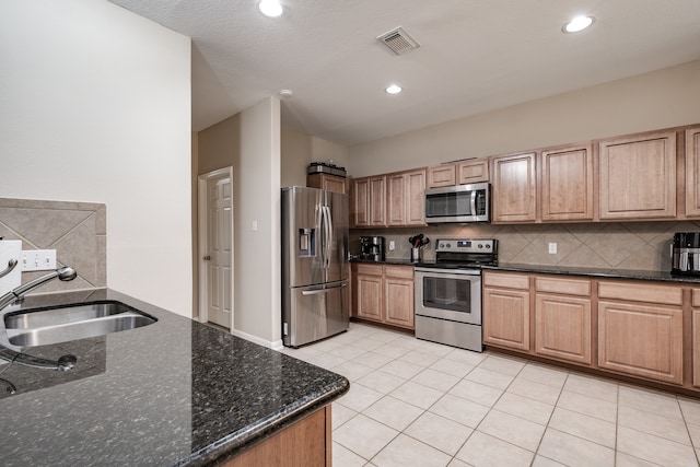 kitchen with dark stone counters, tasteful backsplash, light tile patterned floors, stainless steel appliances, and sink