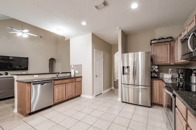 kitchen with dark stone countertops, stainless steel appliances, sink, kitchen peninsula, and ceiling fan