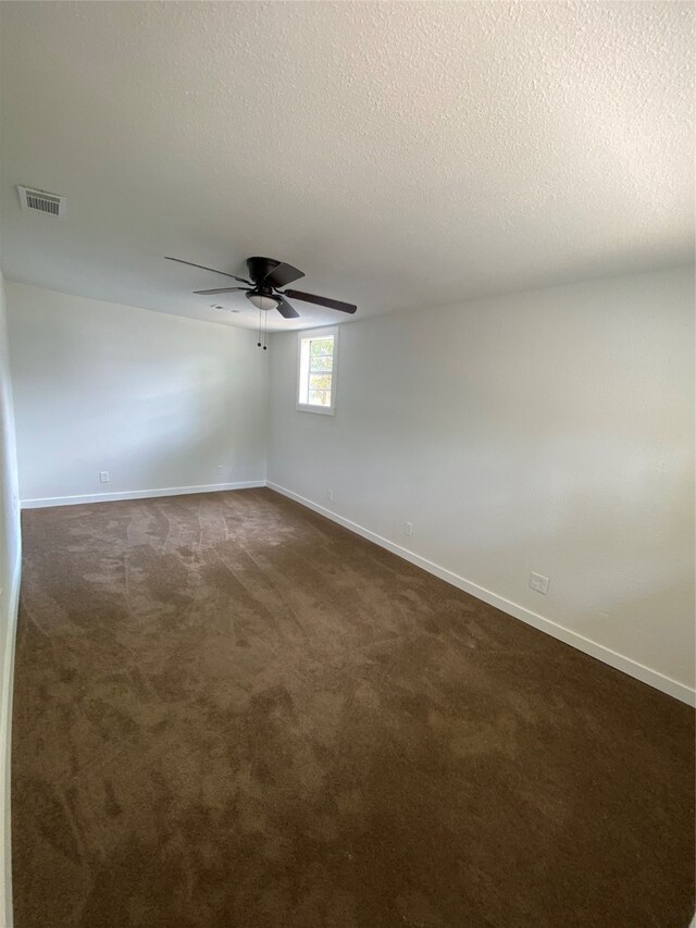 spare room featuring ceiling fan, a textured ceiling, and dark carpet