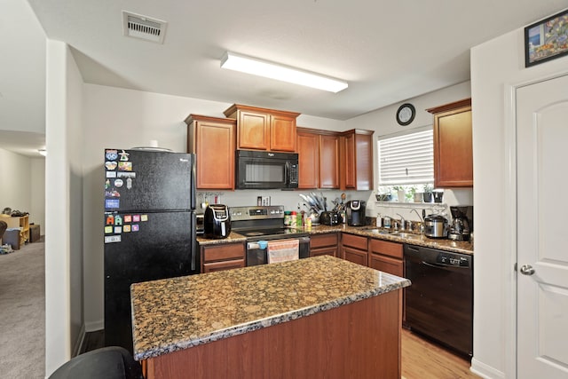 kitchen featuring dark stone counters, sink, light colored carpet, and black appliances