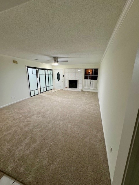 unfurnished living room featuring ceiling fan, a tile fireplace, light carpet, ornamental molding, and a textured ceiling