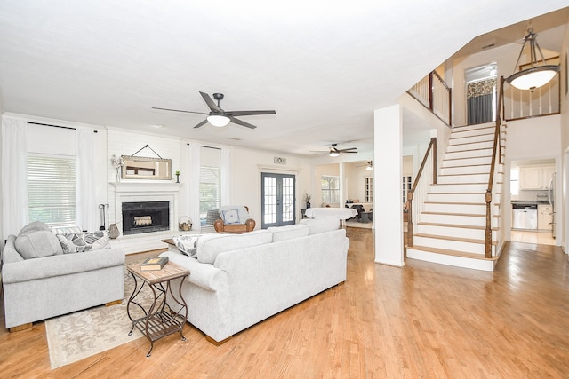 living room featuring ceiling fan, a large fireplace, and light wood-type flooring