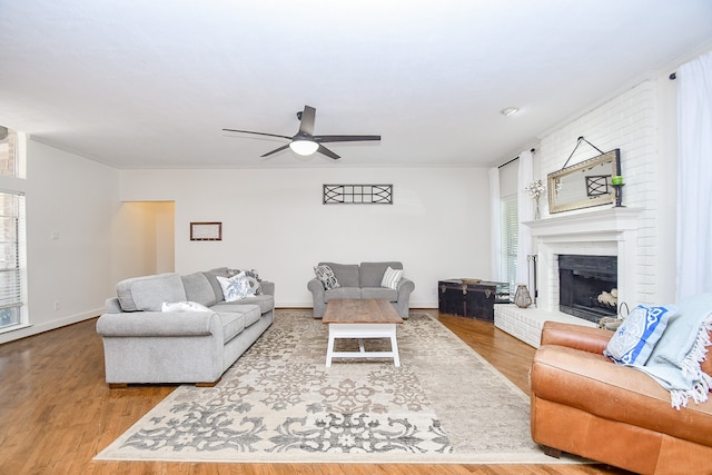 living room featuring ceiling fan, a brick fireplace, hardwood / wood-style floors, and brick wall