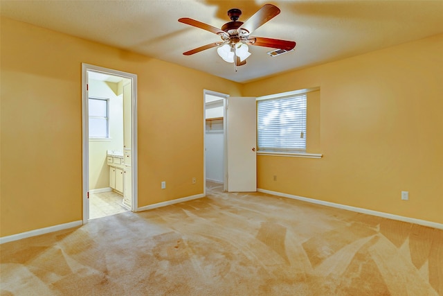 unfurnished bedroom with a walk in closet, ceiling fan, ensuite bath, and light carpet