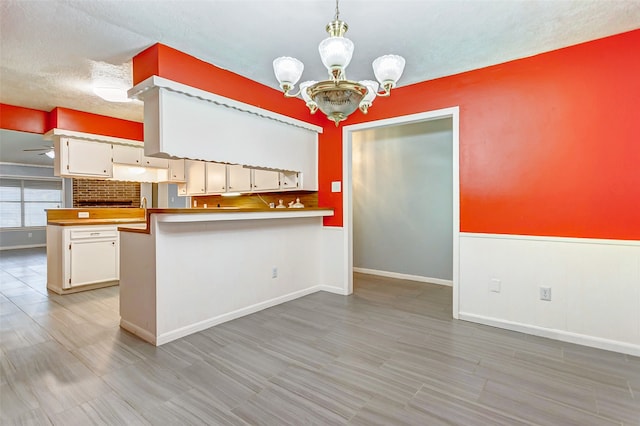 kitchen featuring white cabinetry, kitchen peninsula, pendant lighting, and an inviting chandelier