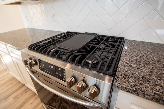 details featuring white cabinets, dark stone countertops, stainless steel range, and light hardwood / wood-style floors