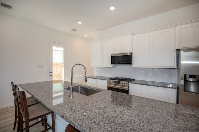 kitchen featuring hardwood / wood-style flooring, stainless steel appliances, sink, dark stone counters, and tasteful backsplash