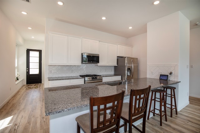 kitchen featuring light wood-type flooring, white cabinets, appliances with stainless steel finishes, and a breakfast bar