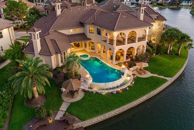 pool featuring an in ground hot tub, a patio area, a water view, and a lawn