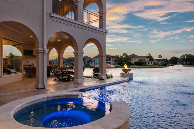 pool featuring a patio, an in ground hot tub, and a water view