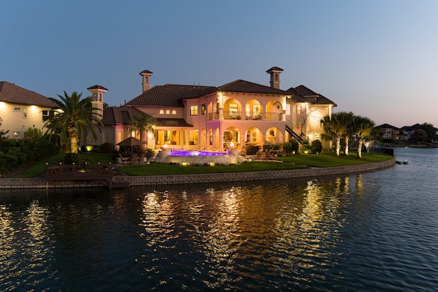 rear view of house featuring a balcony, stucco siding, a water view, a tiled roof, and a patio area