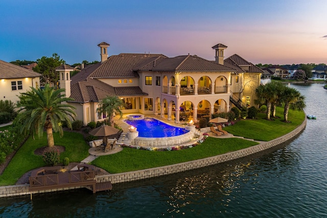 back of property with a balcony, a yard, a patio area, and a water view