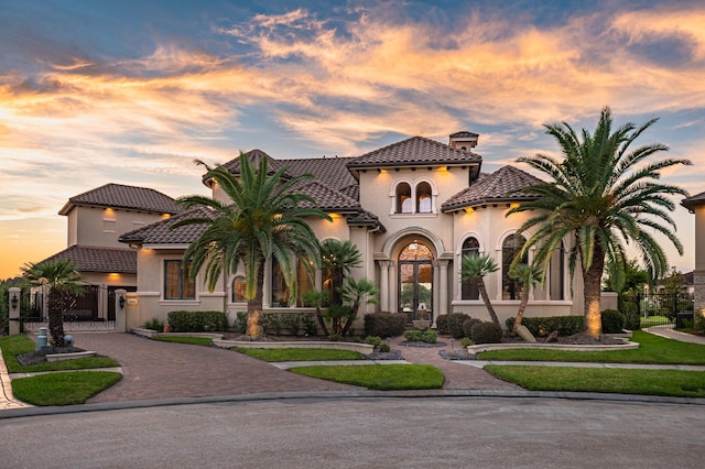 mediterranean / spanish house with a tile roof, a gate, curved driveway, and stucco siding