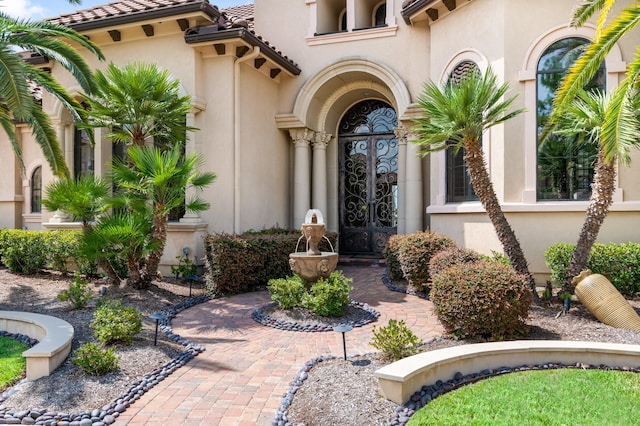 entrance to property featuring a tile roof, french doors, and stucco siding