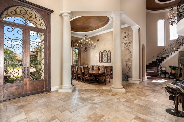 foyer entrance featuring a notable chandelier, stone tile flooring, crown molding, a towering ceiling, and stairs