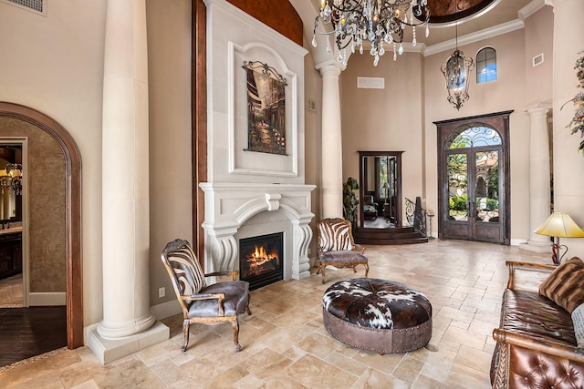 sitting room with baseboards, ornate columns, a high ceiling, stone tile flooring, and a glass covered fireplace