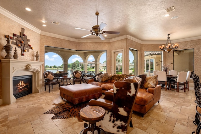 living area featuring stone tile flooring, visible vents, crown molding, and a glass covered fireplace