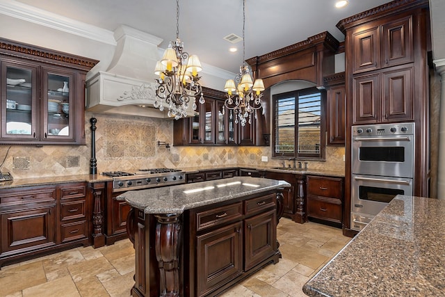 kitchen with crown molding, premium range hood, double oven, stone tile floors, and an inviting chandelier