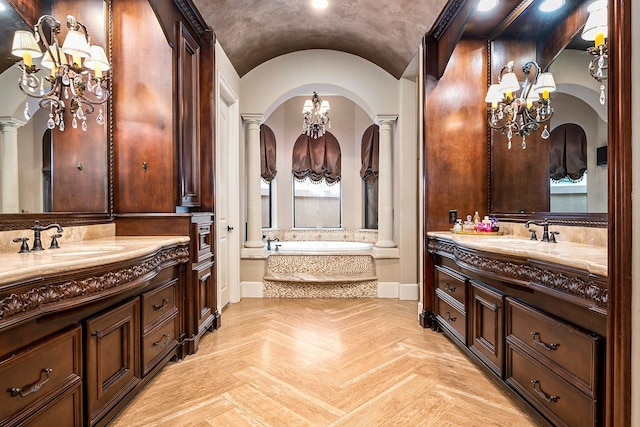 full bath with vaulted ceiling, a notable chandelier, two vanities, and decorative columns