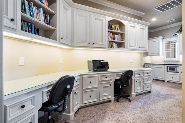 office featuring visible vents, light colored carpet, ornamental molding, and built in desk