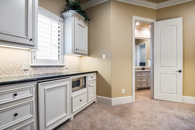 kitchen featuring stainless steel microwave, backsplash, crown molding, baseboards, and light colored carpet