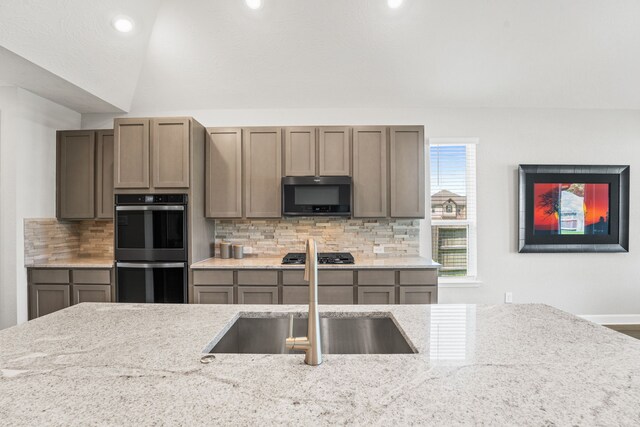 kitchen featuring backsplash, stainless steel appliances, sink, light stone counters, and vaulted ceiling