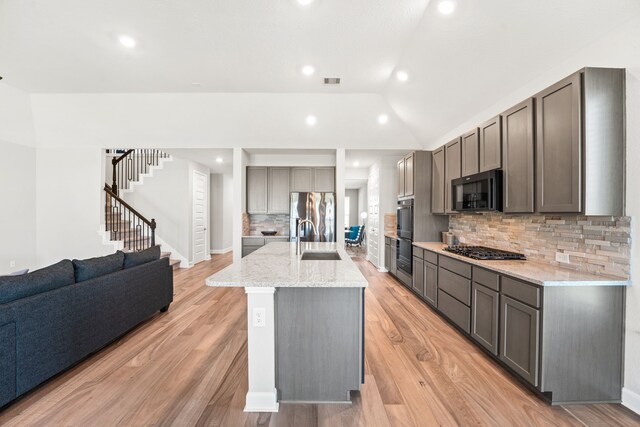 kitchen featuring appliances with stainless steel finishes, light hardwood / wood-style flooring, tasteful backsplash, sink, and a kitchen island with sink