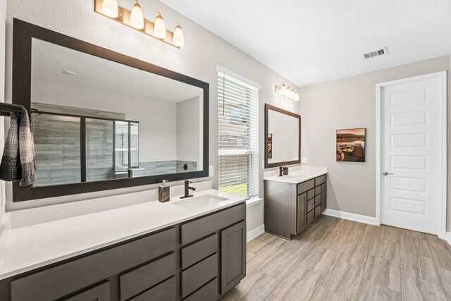 full bathroom featuring baseboards, visible vents, tiled shower, two vanities, and a sink