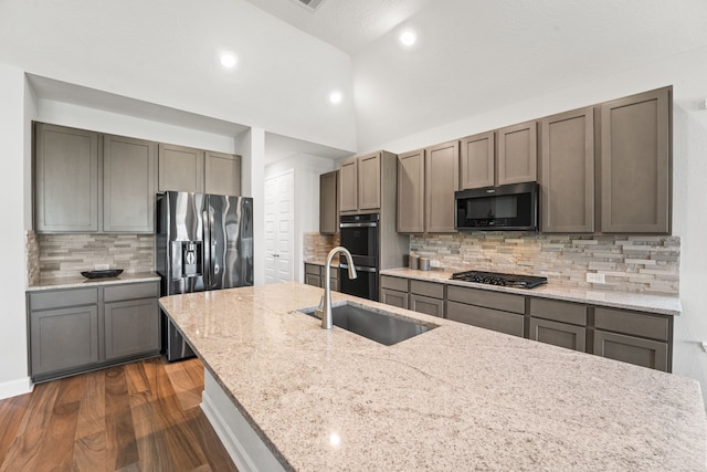 kitchen featuring fridge with ice dispenser, a sink, light stone counters, gas cooktop, and double oven