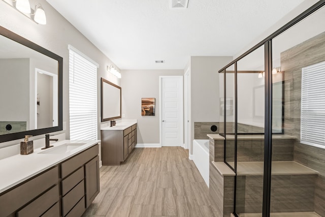 full bath with visible vents, two vanities, a stall shower, a sink, and a garden tub