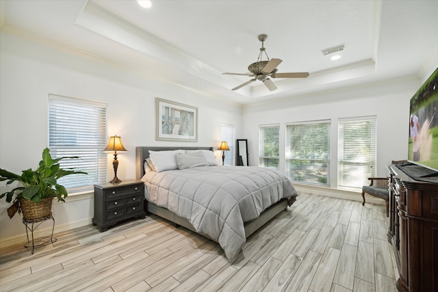 bedroom with ceiling fan, a tray ceiling, and light hardwood / wood-style flooring