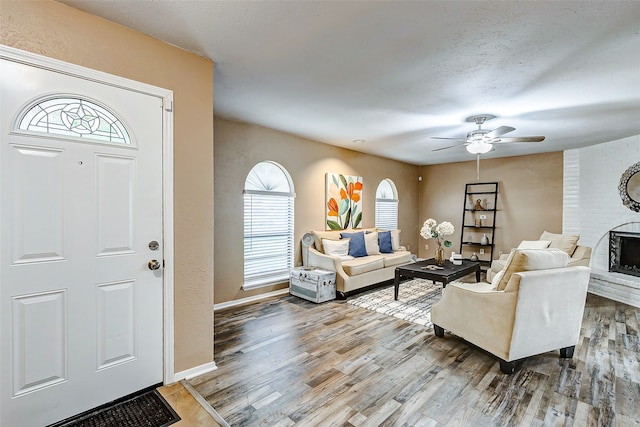 living room featuring hardwood / wood-style floors, brick wall, ceiling fan, and a brick fireplace