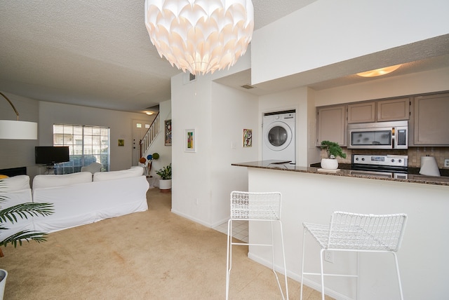 kitchen with decorative backsplash, stacked washer and clothes dryer, a textured ceiling, an inviting chandelier, and stainless steel appliances