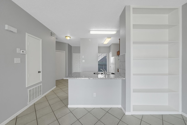 kitchen featuring light tile patterned flooring, sink, kitchen peninsula, and white fridge