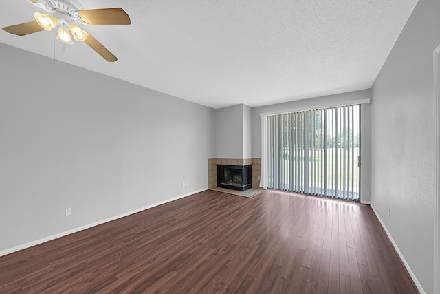 unfurnished living room with ceiling fan, a textured ceiling, a tiled fireplace, and wood-type flooring