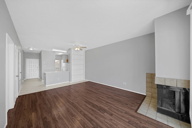 unfurnished living room with light hardwood / wood-style floors, a tile fireplace, and ceiling fan