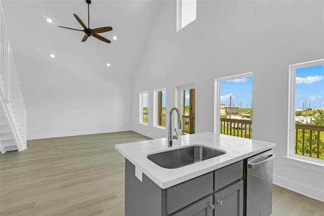 kitchen featuring gray cabinets, light countertops, a kitchen island with sink, a sink, and dishwasher