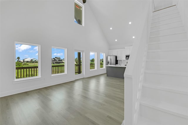 unfurnished living room featuring recessed lighting, light wood-style flooring, a sink, high vaulted ceiling, and baseboards