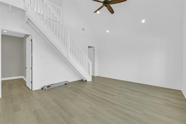 unfurnished living room with ceiling fan, high vaulted ceiling, light wood-style flooring, baseboards, and stairs