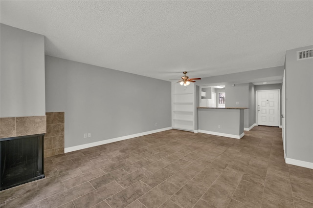 unfurnished living room with ceiling fan, a textured ceiling, tile patterned floors, and a fireplace