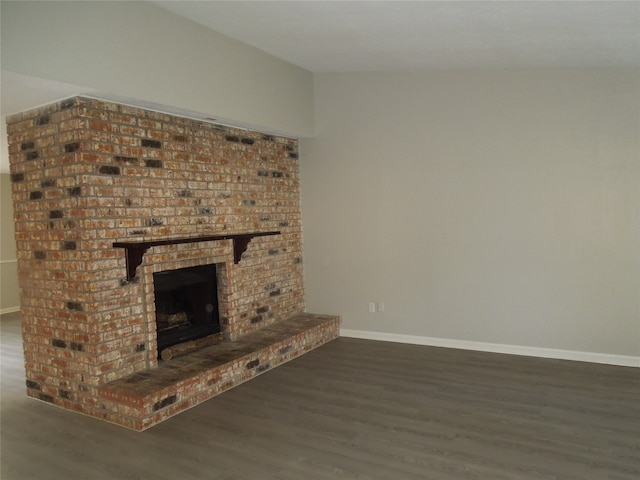 unfurnished living room featuring brick wall, vaulted ceiling, a brick fireplace, and dark hardwood / wood-style flooring