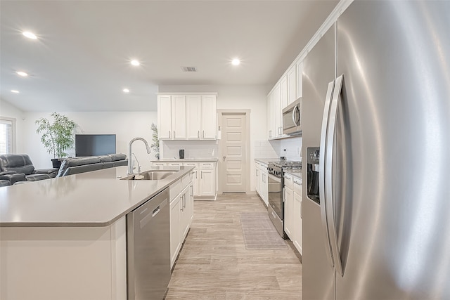 kitchen featuring appliances with stainless steel finishes, backsplash, white cabinetry, sink, and a kitchen island with sink