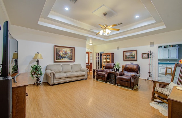 living room featuring ceiling fan, a tray ceiling, and light hardwood / wood-style floors